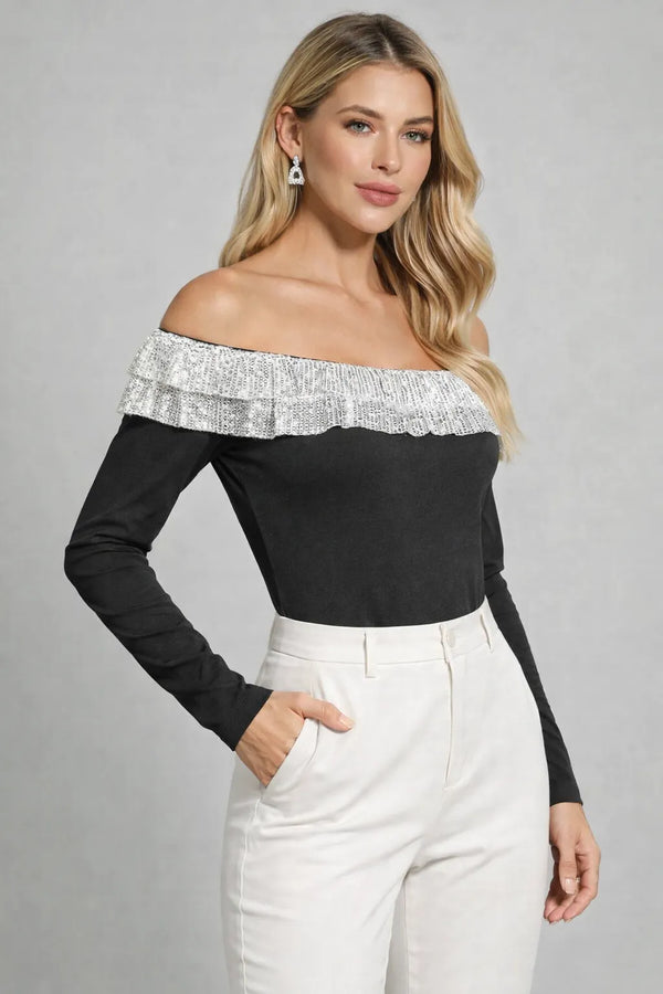 Woman wearing a black off-shoulder top with silver trim and white pants on a gray background