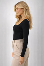 Woman wearing a black long-sleeve top and beige pants against a light gray background