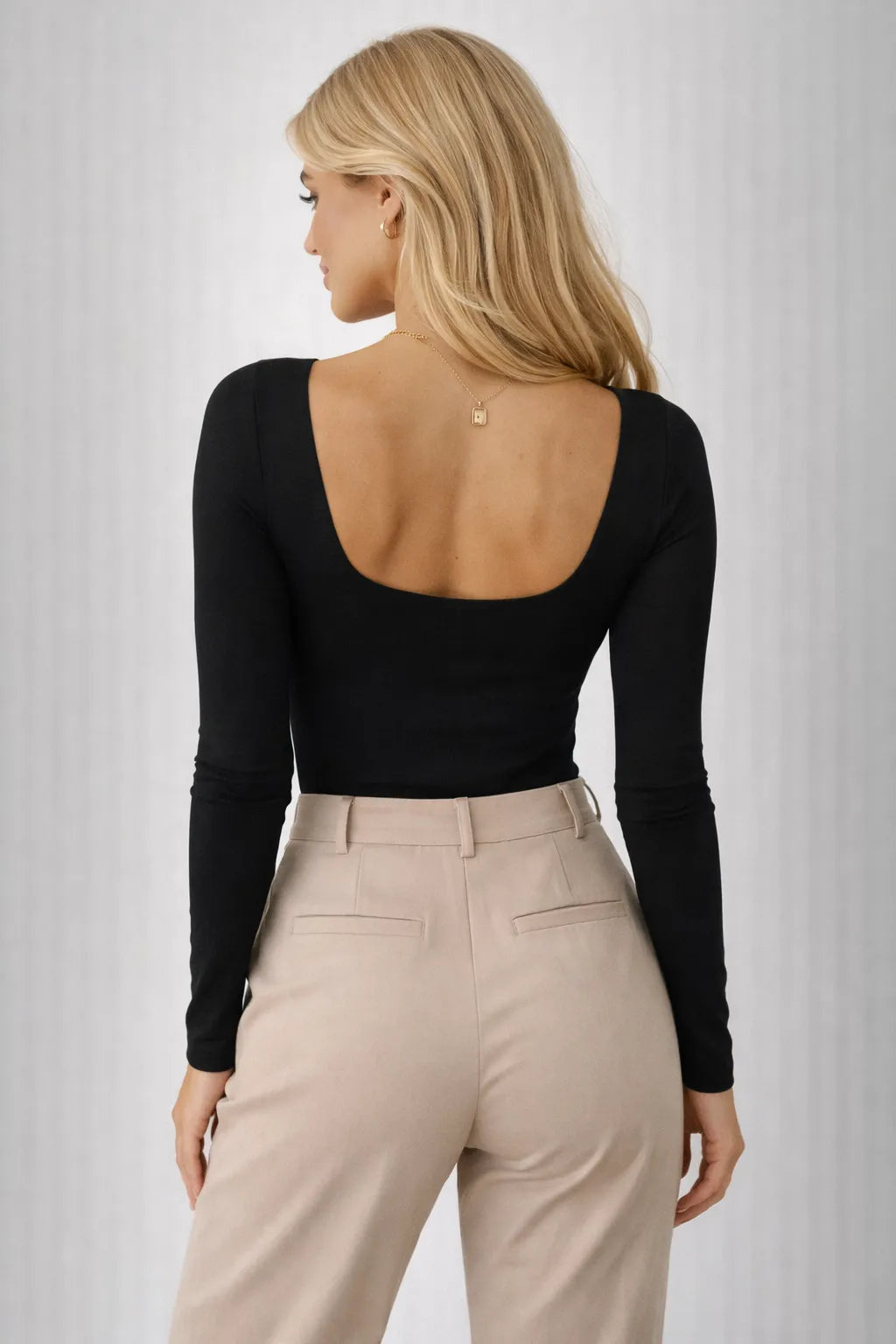 Woman wearing a black long-sleeve top and beige pants on a white background