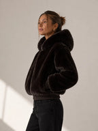 Woman wearing a black fur jacket against a plain background