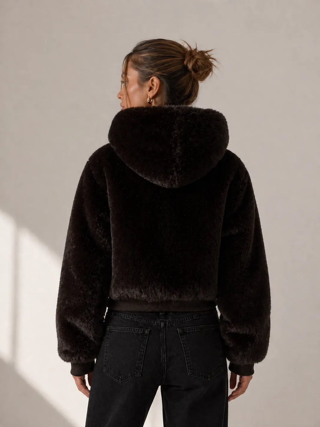 Person wearing a black fur jacket against a neutral background