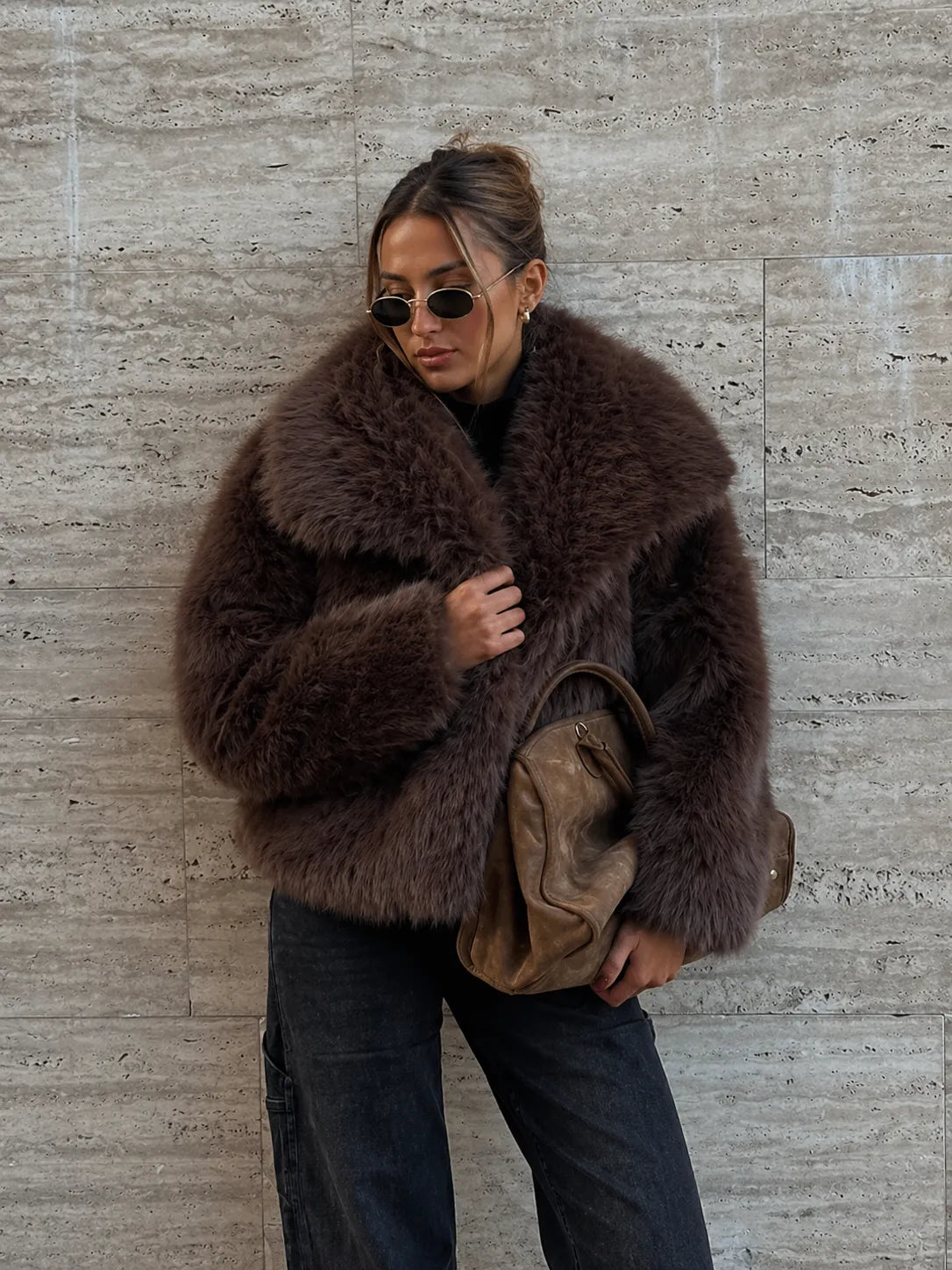 Person wearing a brown fur coat against a textured wall.