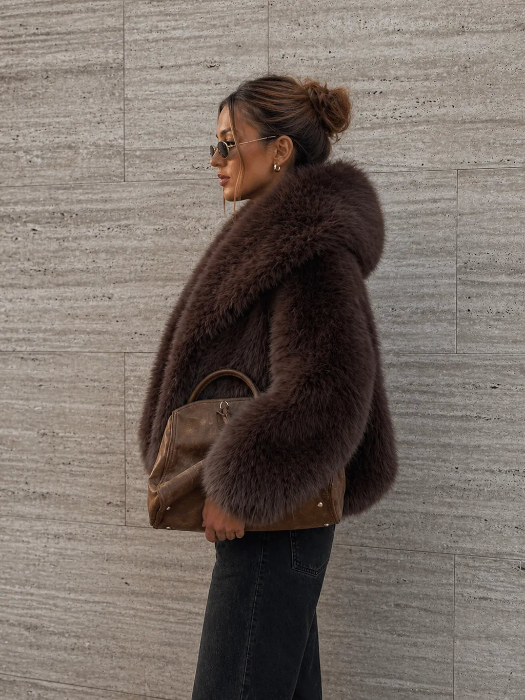 Woman wearing a brown fur coat against a textured wall.