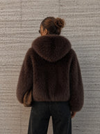 Person wearing a brown fur coat against a textured wall.