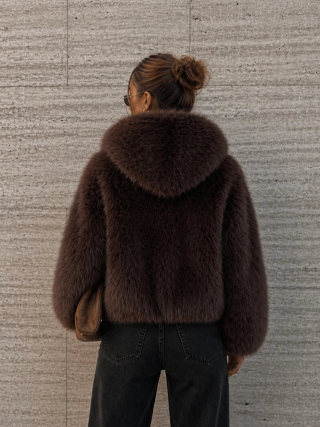 Person wearing a brown fur coat against a textured wall.