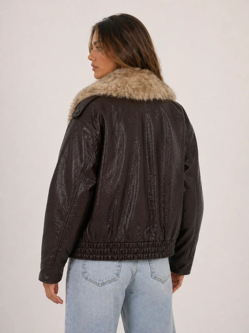 Person wearing a brown leather jacket with fur collar on a plain background