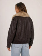 Person wearing a brown leather jacket with fur collar on a plain background