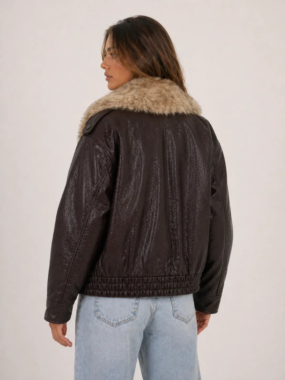 Person wearing a brown leather jacket with fur collar on a plain background