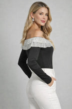 Woman wearing a black off-shoulder top with silver lace details on a gray background
