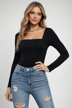 Woman wearing a black long-sleeve top and blue jeans on a plain background