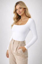 Woman wearing a white long-sleeve top and beige pants on a plain background
