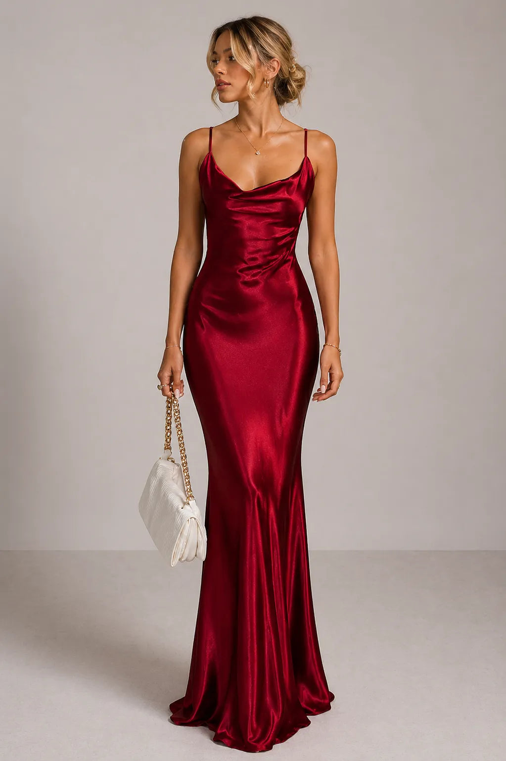 Woman wearing a burgundy satin dress holding a white handbag against a plain background