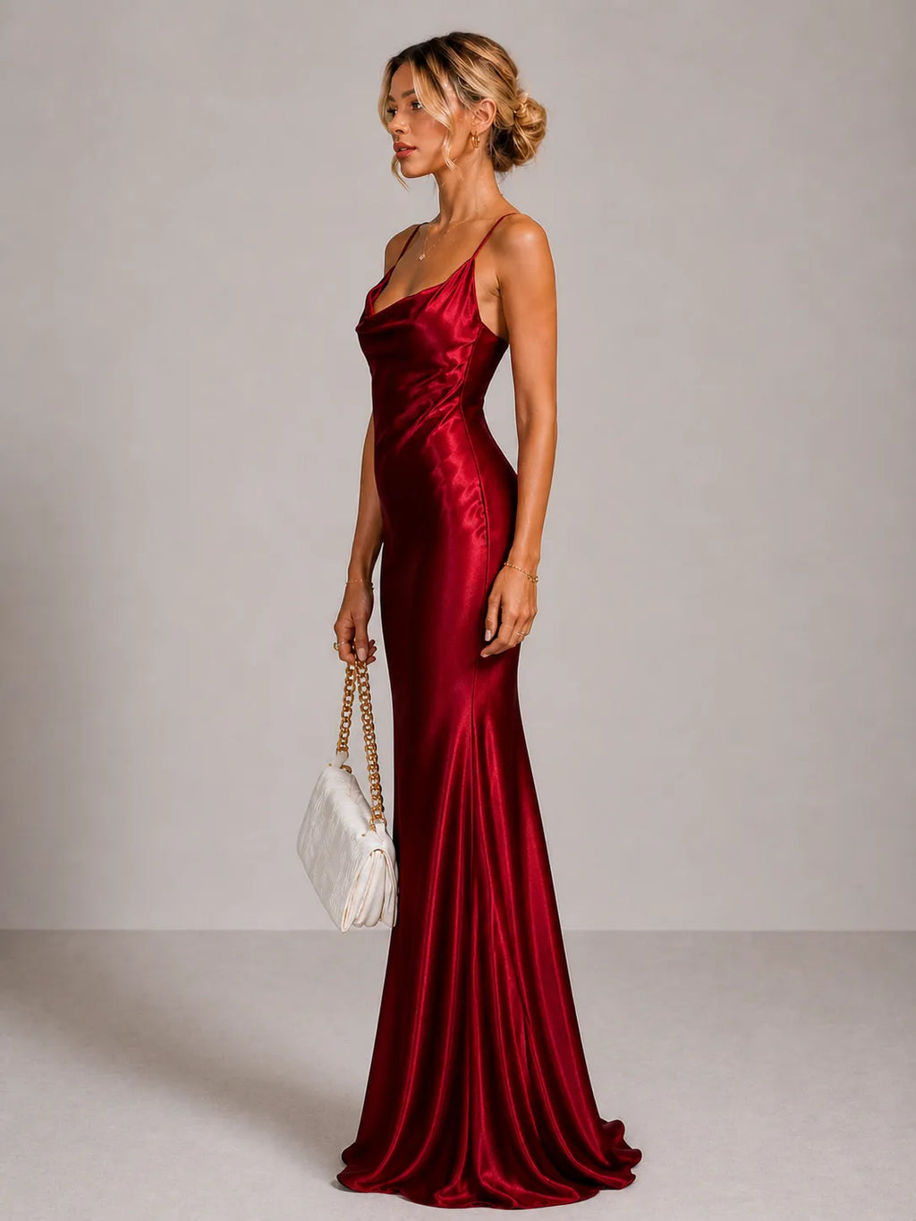 Woman in a red satin dress holding a white handbag against a plain background