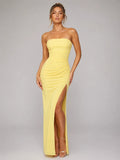 Woman wearing a yellow strapless gown with a high slit on a gray background