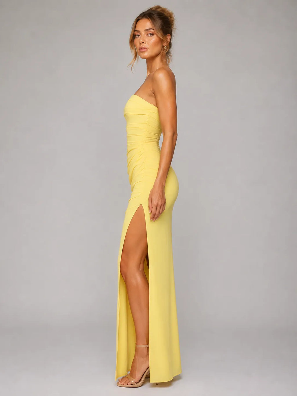 Woman wearing a yellow strapless gown with a high slit on a gray background
