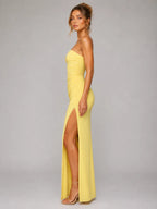 Woman wearing a yellow strapless gown with a high slit on a gray background