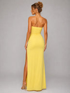 Woman wearing a yellow strapless gown with a high slit on a gray background