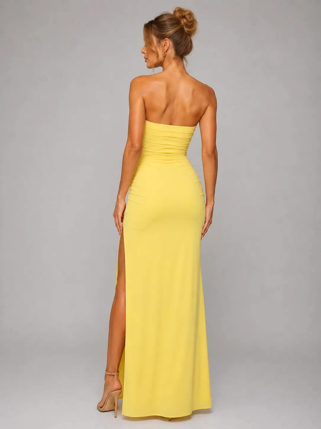 Woman wearing a yellow strapless gown with a high slit on a gray background