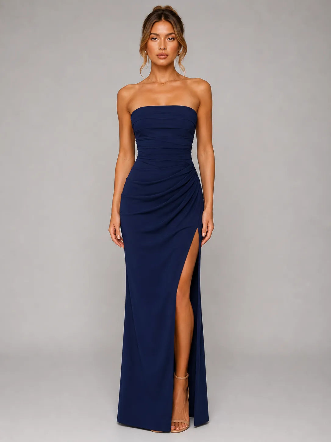 Woman wearing a strapless navy gown with a high slit on a gray background