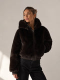Woman wearing a dark brown fur jacket against a plain background