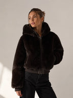 Woman wearing a dark brown fur jacket against a plain background