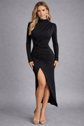 Woman wearing a black long-sleeve dress with a high slit on a gray background