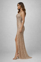 Woman wearing a sparkly gold evening gown with a slit on a gray background