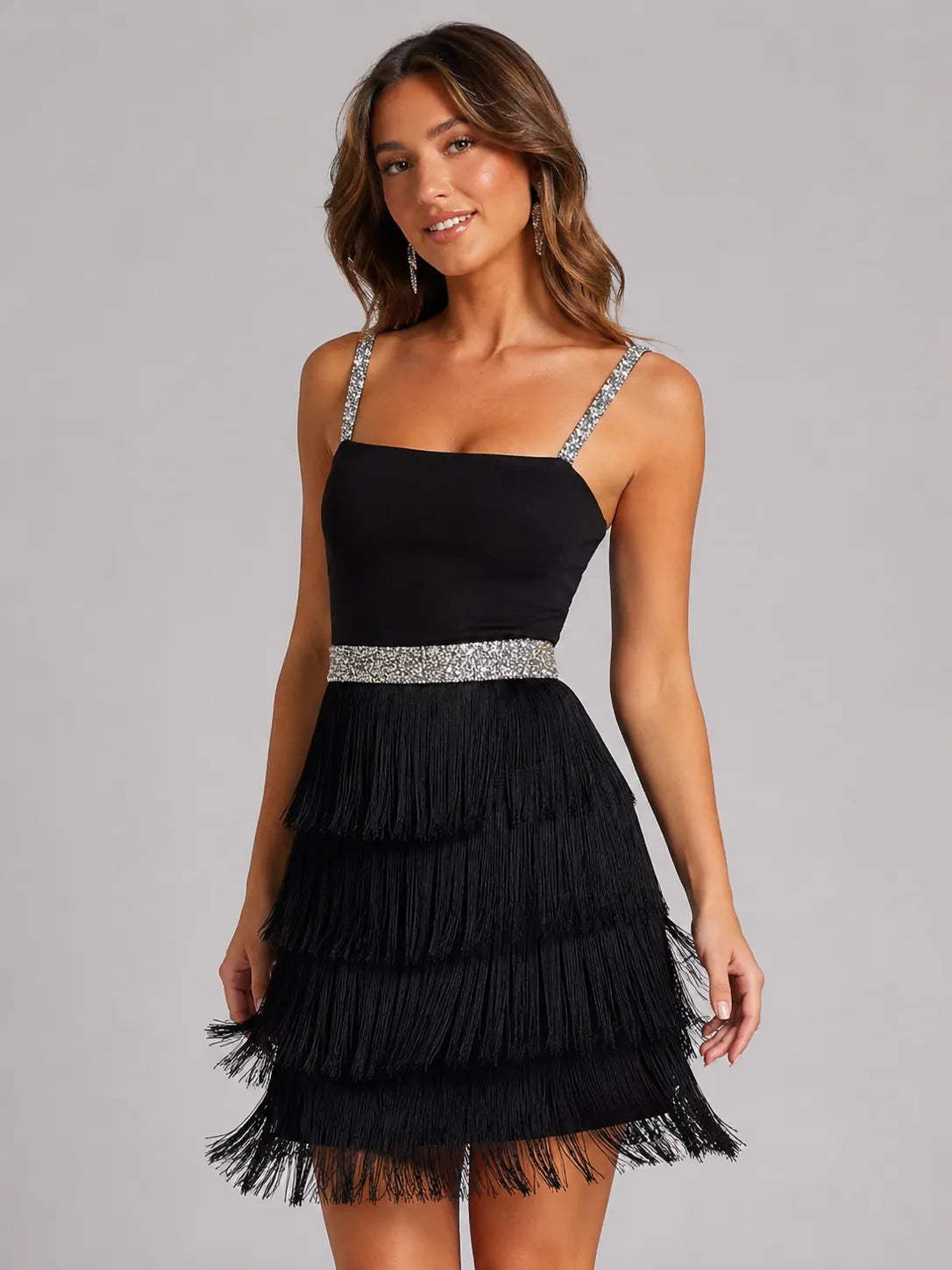 Black dress with fringe details and silver waistband worn by a model on a gray background
