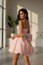 Woman wearing a pink dress with a bow detail in a bright room.